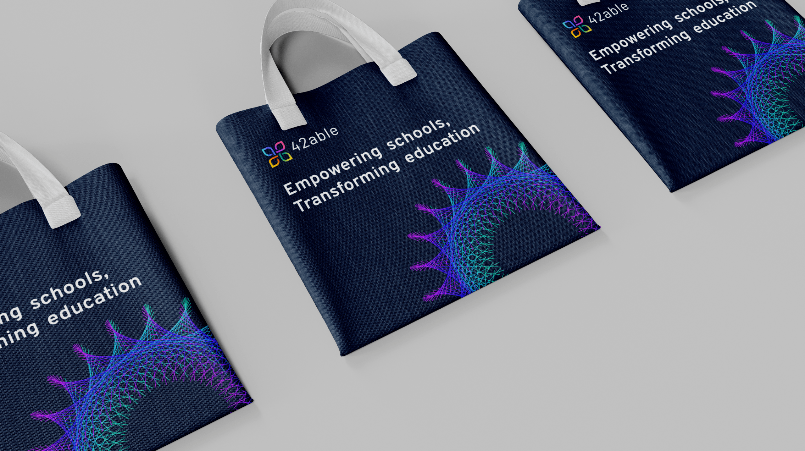 Three dark blue tote bags with white handles display the text “Empowering schools. Transforming education.” and a geometric, colorful spiral design—perfect for celebrating your school’s rebranding or digital marketing initiatives.